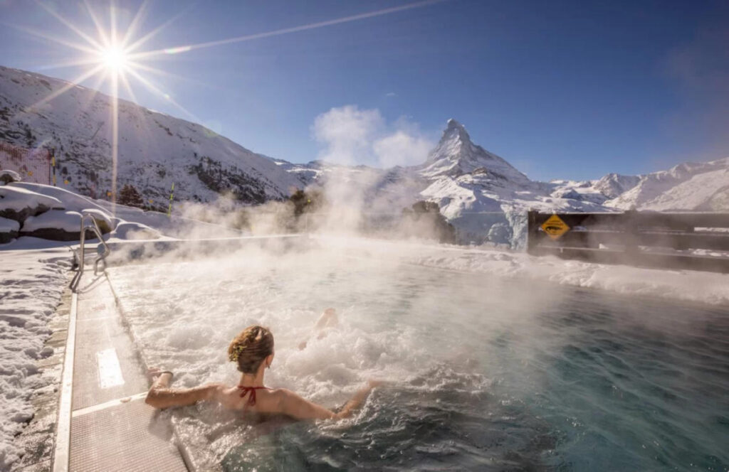 woman relaxing in hot tub looking at the Matterhorn on a sunny winter day